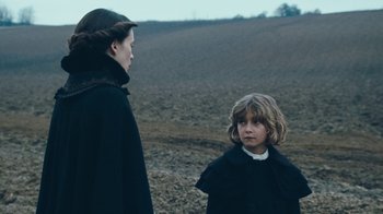 Movie still from “The Childhood of a Leader” (2015), directed by Brady Corbet – A woman and a child standing in a field; Medium shot, Over the shoulder angle