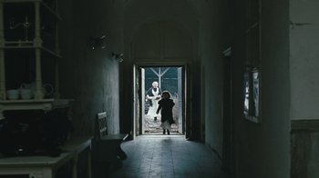Movie still from “The Childhood of a Leader” (2015), directed by Brady Corbet – A person standing in a hallway with a person standing in the doorway; Wide shot, Low angle