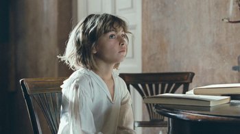 Movie still from “The Childhood of a Leader” (2015), directed by Brady Corbet – A young girl sitting at a table looking up; Medium shot, Low angle