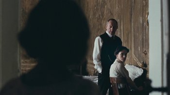 Movie still from “The Childhood of a Leader” (2015), directed by Brady Corbet – A man and a woman standing next to each other in a room; Medium shot, Over the shoulder angle
