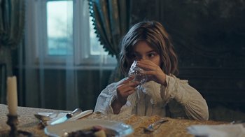 Movie still from “The Childhood of a Leader” (2015), directed by Brady Corbet – A young girl sitting at a table eating a sandwich; Medium shot, Over the shoulder angle