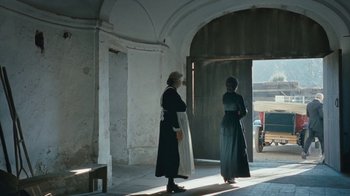 Movie still from “The Childhood of a Leader” (2015), directed by Brady Corbet – Two women dressed in period clothing stand in front of an archway; Wide shot, Low angle