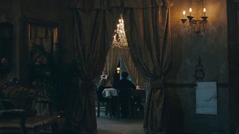 Movie still from “The Childhood of a Leader” (2015), directed by Brady Corbet – People are sitting at a table in front of a chandelier; Wide shot, Over the shoulder angle