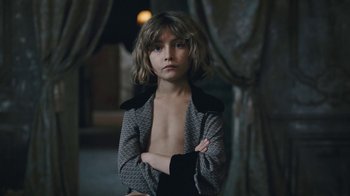 Movie still from “The Childhood of a Leader” (2015), directed by Brady Corbet – A young boy with his arms crossed in front of a curtain; Medium shot, High angle