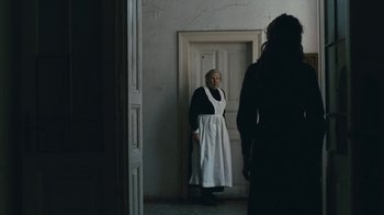Movie still from “The Childhood of a Leader” (2015), directed by Brady Corbet – An old woman in a black dress and a white apron; Wide shot, Over the shoulder angle