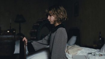 Movie still from “The Childhood of a Leader” (2015), directed by Brady Corbet – A young girl standing in a dark room next to a bed; Medium shot, Over the shoulder angle