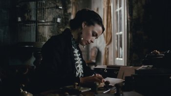 Movie still from “The Childhood of a Leader” (2015), directed by Brady Corbet – A woman sitting at a table writing on a piece of paper; Medium shot, High angle