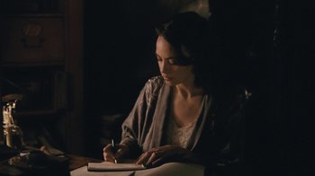 Movie still from “The Childhood of a Leader” (2015), directed by Brady Corbet – A woman writing on a piece of paper in a dark room; Medium shot, High angle