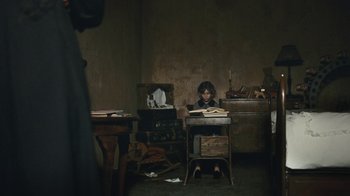 Movie still from “The Childhood of a Leader” (2015), directed by Brady Corbet – A woman sitting at a table with a book in her hands; Wide shot, High angle