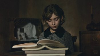 Movie still from “The Childhood of a Leader” (2015), directed by Brady Corbet – A young girl is reading a book on a table; Close Up shot, High angle