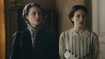 Movie still from “The Childhood of a Leader” (2015), directed by Brady Corbet – Two women standing next to each other in front of a book shelf; Close Up shot, Over the shoulder angle