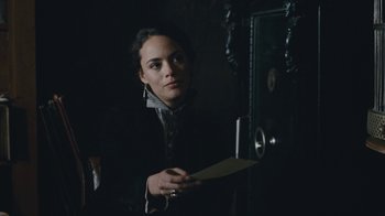Movie still from “The Childhood of a Leader” (2015), directed by Brady Corbet – A woman holding a paper in front of a door; Medium shot, Over the shoulder angle
