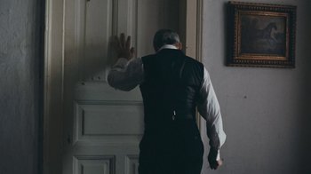 Movie still from “The Childhood of a Leader” (2015), directed by Brady Corbet – An older man wearing a suit and tie is entering a door; Medium shot, Over the shoulder angle