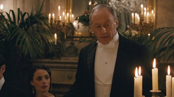 Movie still from “The Childhood of a Leader” (2015), directed by Brady Corbet – An older man in a tuxedo standing in front of a candle; Medium shot, Over the shoulder angle