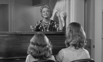 Movie still from “The Children's Hour” (1961), directed by William Wyler – Two women are watching a woman play a musical instrument; Medium shot, Over the shoulder angle