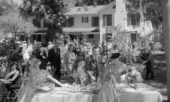 Movie still from “The Children's Hour” (1961), directed by William Wyler – A group of people sitting around a table with cake; Wide shot, High angle