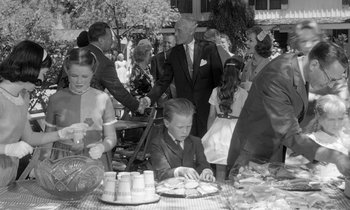 Movie still from “The Children's Hour” (1961), directed by William Wyler – A black and white photo of a group of people at an outdoor party; Medium shot, Over the shoulder angle