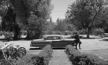 Movie still from “The Children's Hour” (1961), directed by William Wyler – An old photo of a man standing next to an old car; Extreme Wide shot, High angle