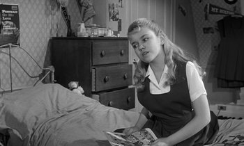Movie still from “The Children's Hour” (1961), directed by William Wyler – A young girl sitting on a bed looking at a magazine; Medium shot, High angle