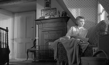 Movie still from “The Children's Hour” (1961), directed by William Wyler – A woman sitting on a couch in a living room next to a fire place; Medium shot, Low angle