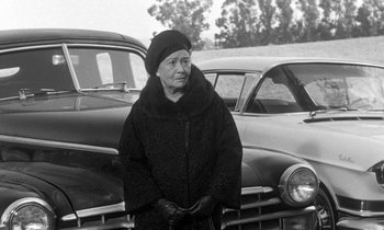 Movie still from “The Children's Hour” (1961), directed by William Wyler – An older woman standing in front of two old cars; Medium shot, Low angle