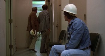 Movie still from “The China Syndrome” (1979), directed by James Bridges – A man in a hard hat sitting in front of two other men; Wide shot, Over the shoulder angle