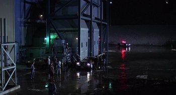 Movie still from “The China Syndrome” (1979), directed by James Bridges – A group of people standing next to a car in the rain; Extreme Wide shot, High angle