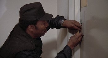 Movie still from “The China Syndrome” (1979), directed by James Bridges – A man in a black hat is fixing a lock on a wall; Close Up shot, High angle