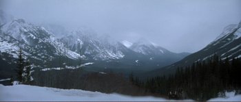 Movie still from “The Claim” (2000), directed by Michael Winterbottom – A snowy mountain range with trees in the foreground; Extreme Wide shot, High angle