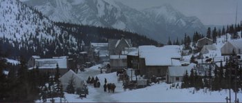 Movie still from “The Claim” (2000), directed by Michael Winterbottom – A group of people riding horses in the snow near a mountain range; Extreme Wide shot, High angle