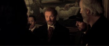 Movie still from “The Claim” (2000), directed by Michael Winterbottom – A group of men standing next to each other in front of a painting; Medium shot, Over the shoulder angle
