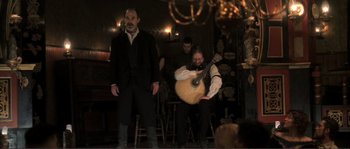 Movie still from “The Claim” (2000), directed by Michael Winterbottom – A group of men in a room with a guitar; Wide shot, Low angle