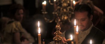 Movie still from “The Claim” (2000), directed by Michael Winterbottom – Many candles on the table in front of the chandelier; Medium shot, Over the shoulder angle