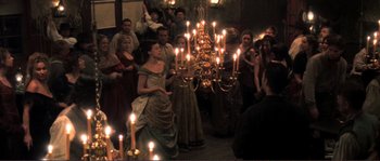 Movie still from “The Claim” (2000), directed by Michael Winterbottom – A group of people standing around a room with lit candles; Wide shot, High angle