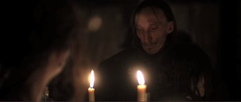 Movie still from “The Claim” (2000), directed by Michael Winterbottom – A man standing in front of two lit candles; Close Up shot, Over the shoulder angle