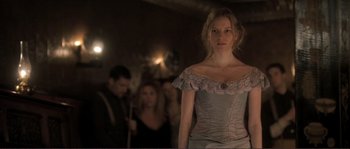 Movie still from “The Claim” (2000), directed by Michael Winterbottom – A woman standing in front of a group of people; Medium shot, Over the shoulder angle
