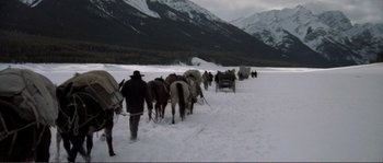 Movie still from “The Claim” (2000), directed by Michael Winterbottom – A group of horses being led by a man in the snow; Wide shot, High angle