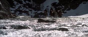 Movie still from “The Claim” (2000), directed by Michael Winterbottom – A group of people riding horses across a river; Wide shot, High angle