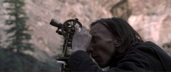 Movie still from “The Claim” (2000), directed by Michael Winterbottom – A man looking through a telescope in the woods; Close Up shot, High angle