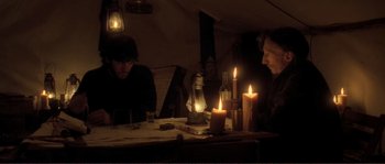 Movie still from “The Claim” (2000), directed by Michael Winterbottom – Two people sitting at a table with candles; Medium shot, Over the shoulder angle