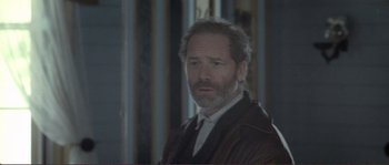 Movie still from “The Claim” (2000), directed by Michael Winterbottom – A man with a beard is standing in front of a window; Close Up shot, Over the shoulder angle