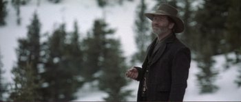 Movie still from “The Claim” (2000), directed by Michael Winterbottom – A man in a hat and a jacket holding a cigar; Medium shot, Low angle