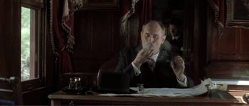 Movie still from “The Claim” (2000), directed by Michael Winterbottom – A man sitting at a table smoking a cigarette; Medium shot, Low angle