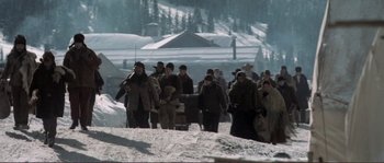 Movie still from “The Claim” (2000), directed by Michael Winterbottom – A group of people walking in the snow near some trees; Wide shot, High angle