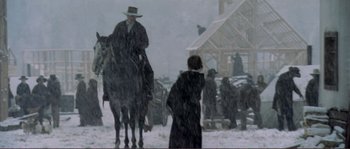 Movie still from “The Claim” (2000), directed by Michael Winterbottom – A man riding a horse in the snow with a woman; Wide shot, Low angle