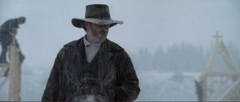 Movie still from “The Claim” (2000), directed by Michael Winterbottom – A man wearing a hat standing in the snow; Medium shot, Low angle