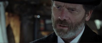 Movie still from “The Claim” (2000), directed by Michael Winterbottom – A person wearing a suit and a hat; Close Up shot, Over the shoulder angle