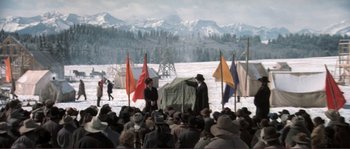 Movie still from “The Claim” (2000), directed by Michael Winterbottom – A group of people standing in the snow with flags; Extreme Wide shot, High angle