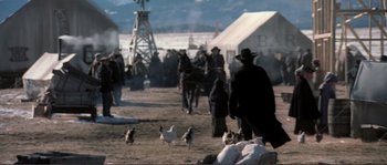 Movie still from “The Claim” (2000), directed by Michael Winterbottom – A group of people standing next to chickens in a field; Wide shot, High angle
