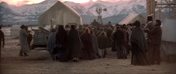 Movie still from “The Claim” (2000), directed by Michael Winterbottom – A group of people standing in front of a windmill; Extreme Wide shot, High angle